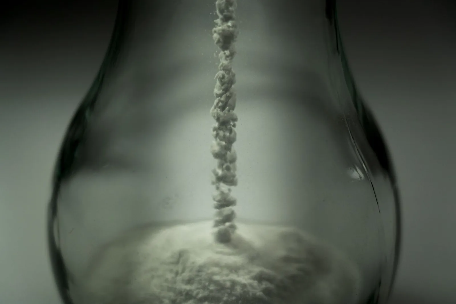 Fine white PDRN powder flowing into a glass vessel